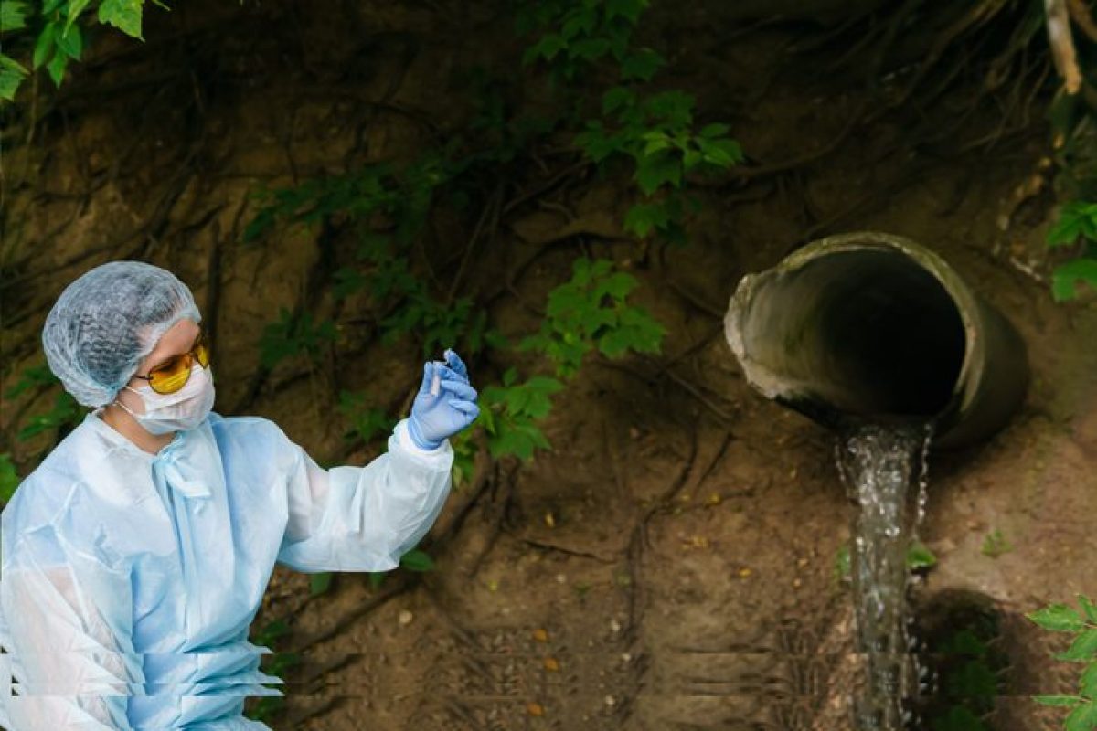 female ecologist or epidemiologist looking at a test tube with sample of water on a background of sewer coming out of the ground